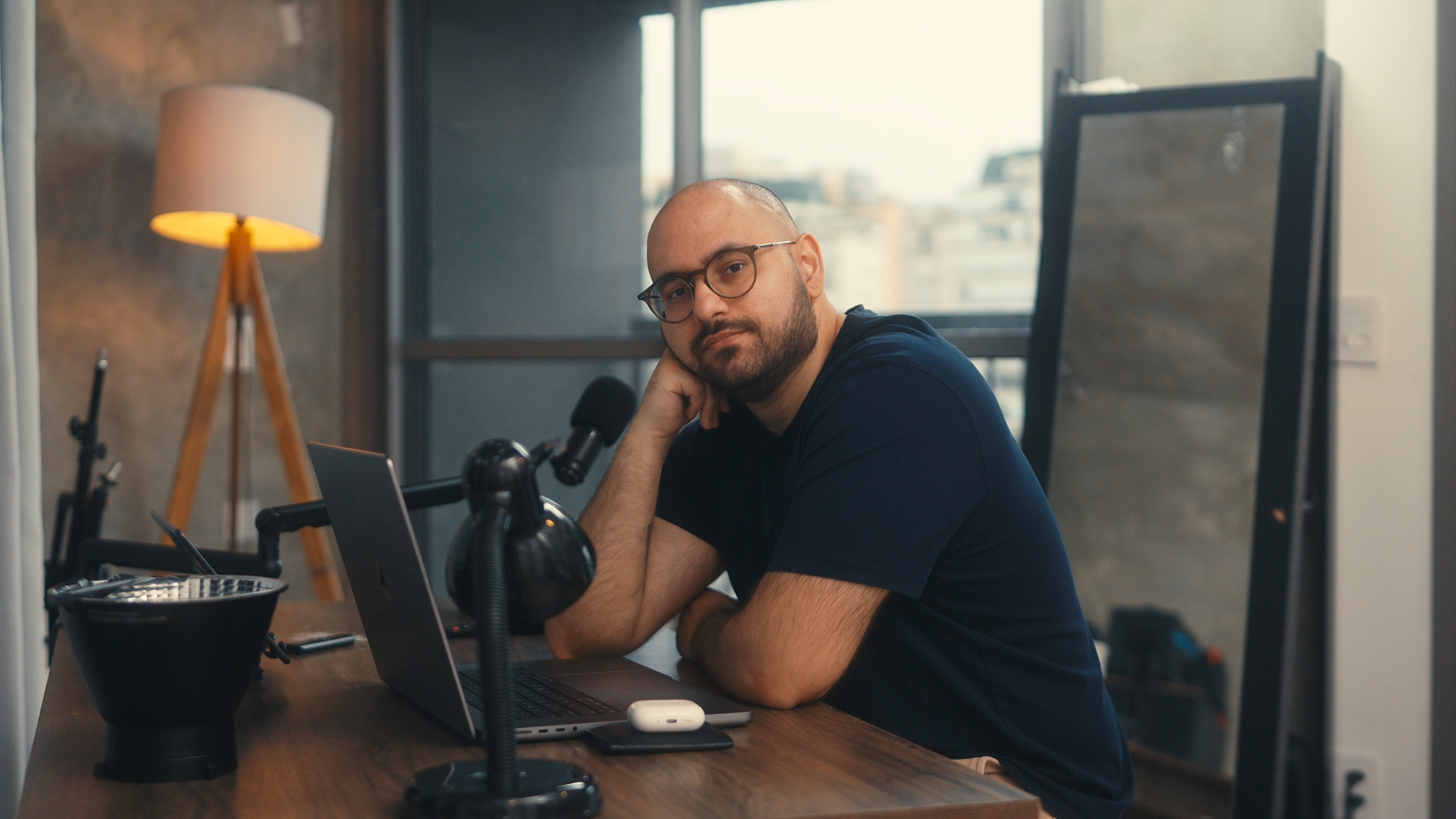 Nicolai à sua mesa de trabalho, com laptop, microfone e a cidade ao fundo